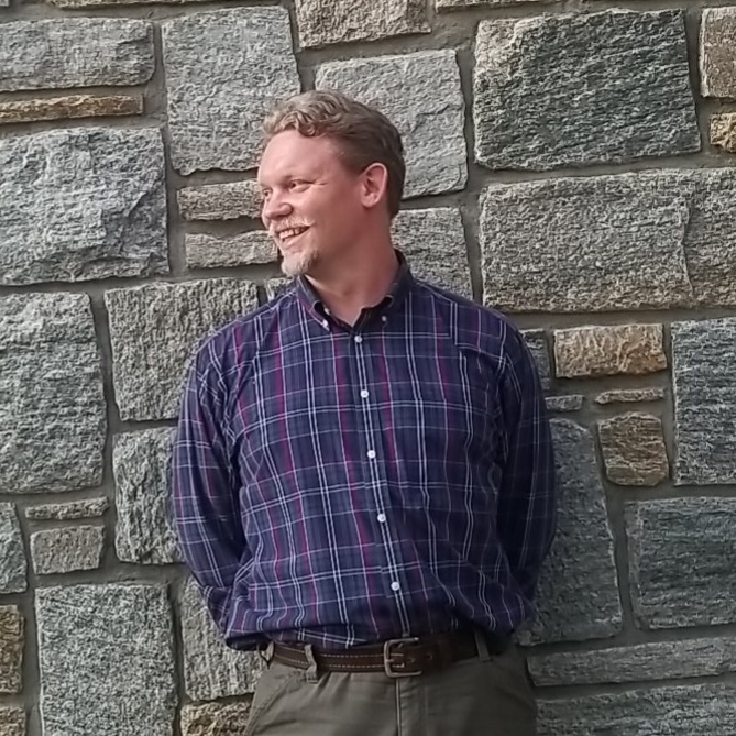 Paul Motten standing in a collared shirt against a stone wall