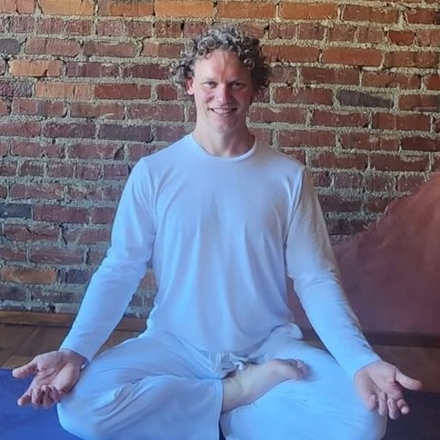 Paul Motten seated cross-legged in white yoga teaching attire